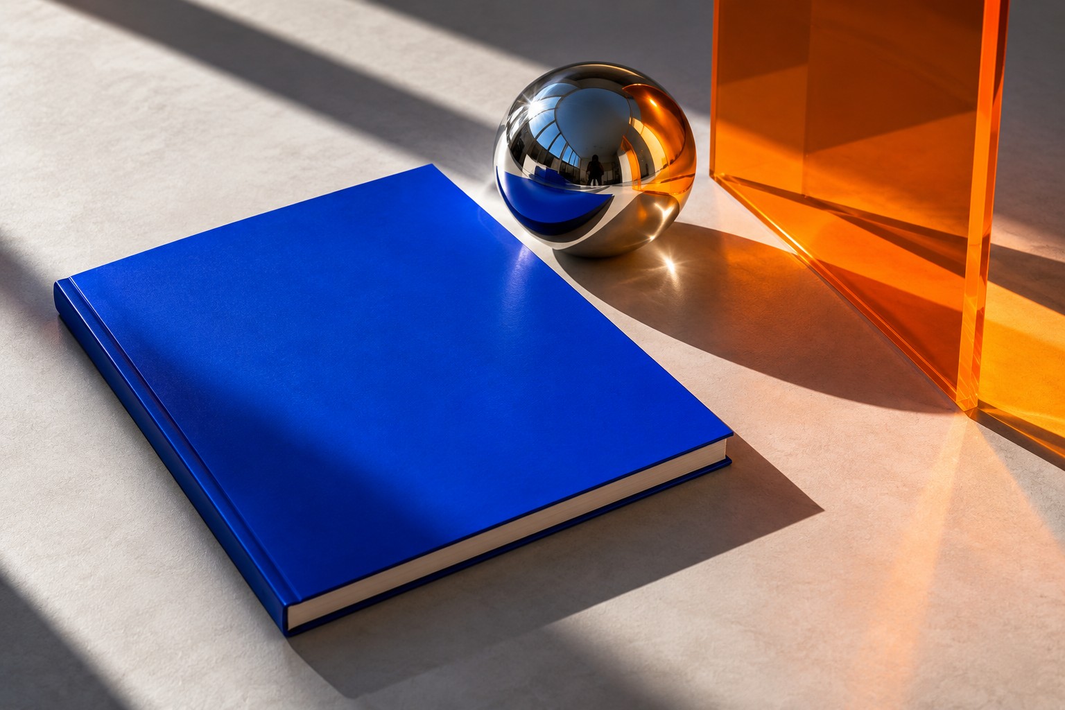 Sculptural creative still life with a cobalt magazine, chrome sphere and orange acrylic